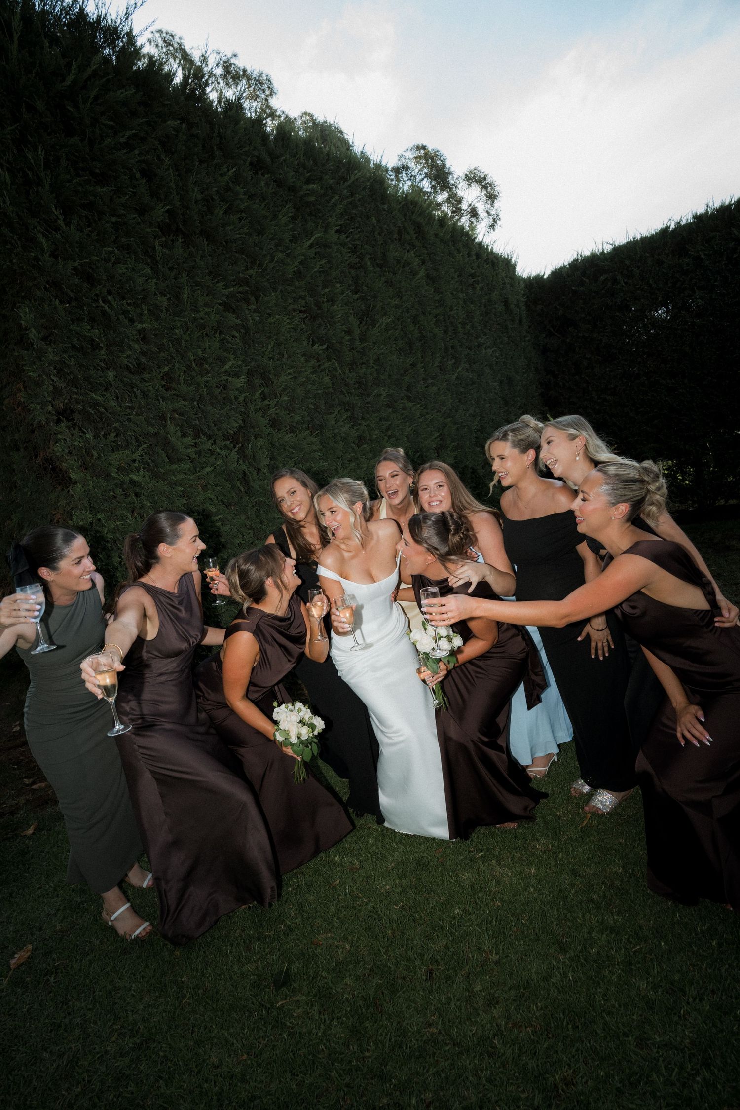 Wedding party poses for fun falling domino effect photo on grass at sunset.