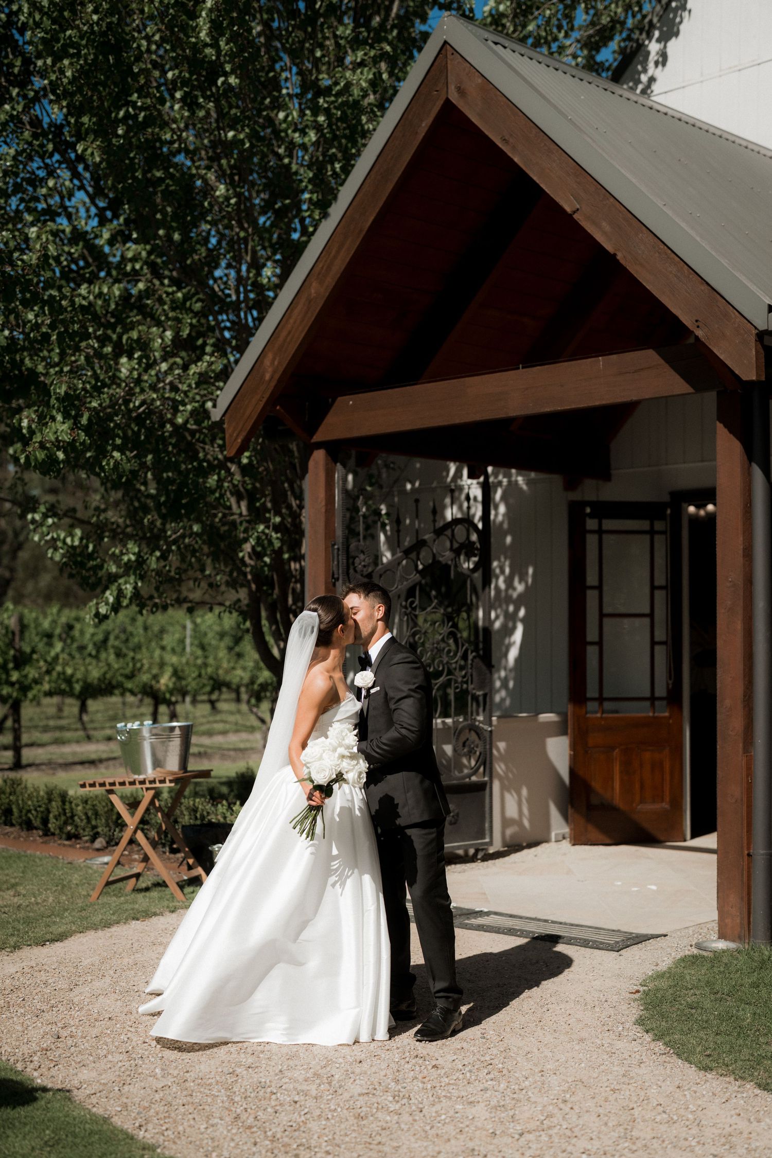 A wedding couple shares a moment outside a rustic chapel entrance on a sunny day.