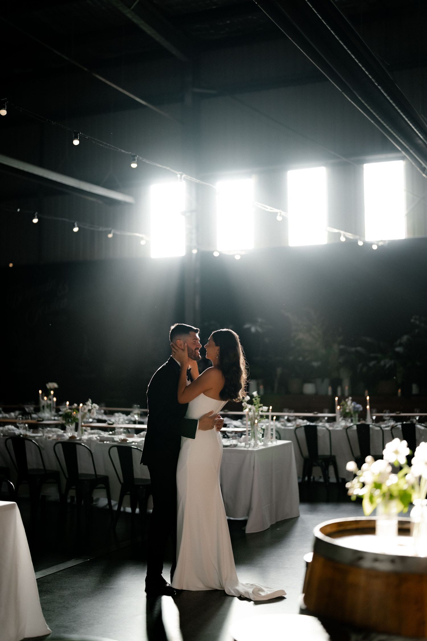 A couple shares their first dance in an elegant reception venue with dramatic backlighting and round tables.