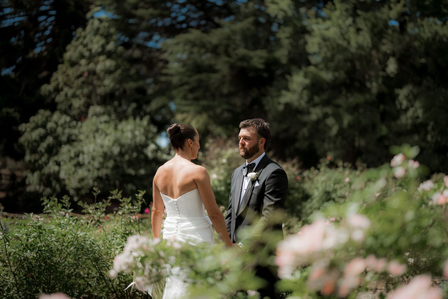 Bride and groom share a romantic moment surrounded by lush gardens and pink flowers.