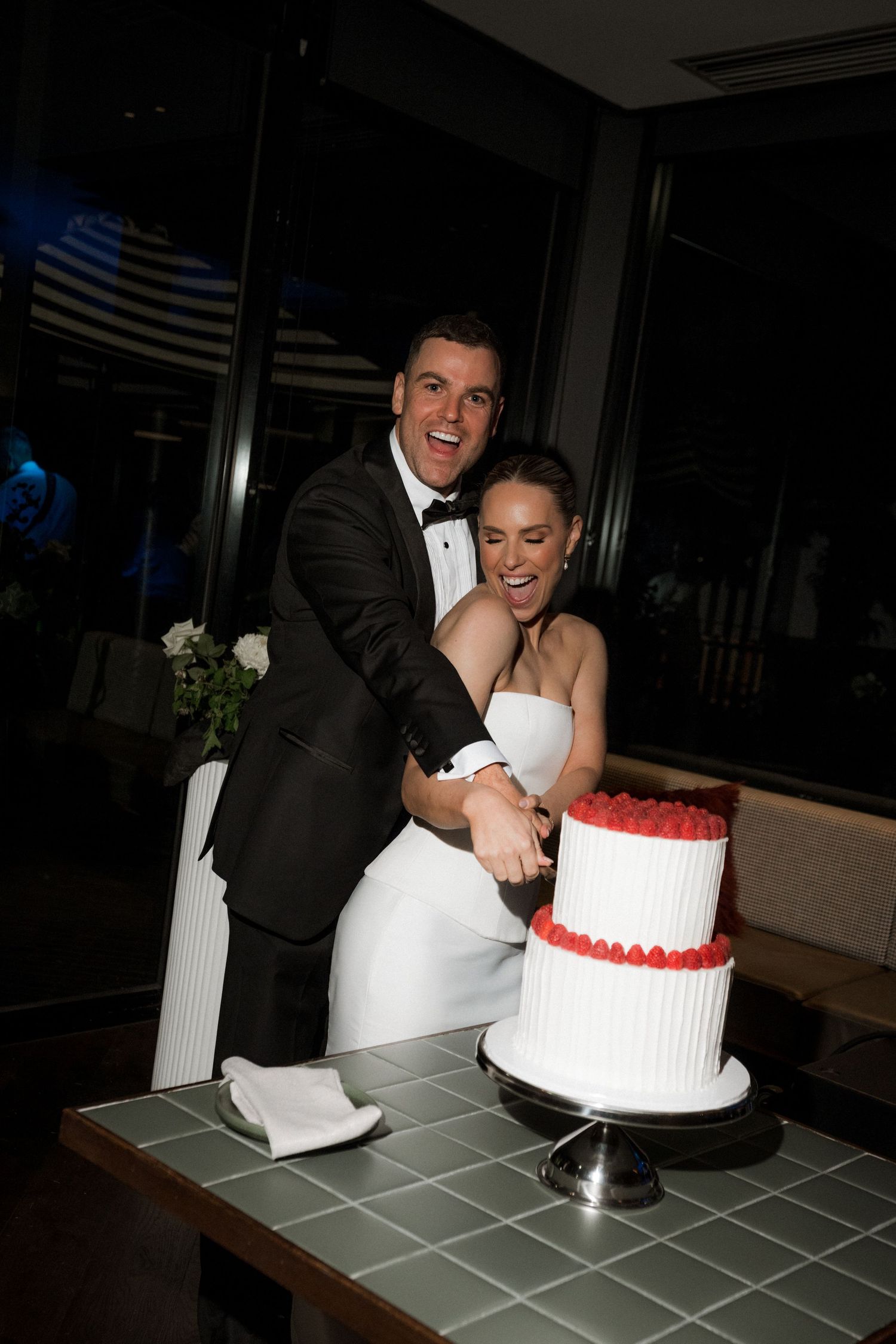 Wedding couple cuts their two-tiered white and red cake at modern reception venue.