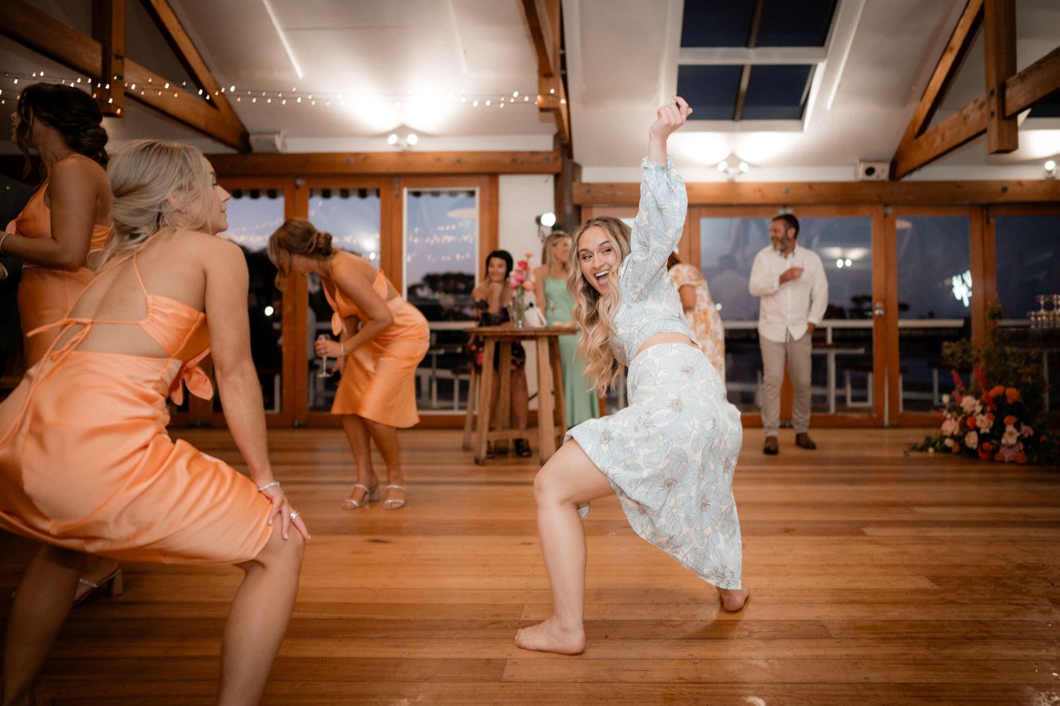 Wedding reception dance floor moments captured on rustic wooden floor with warm lighting.