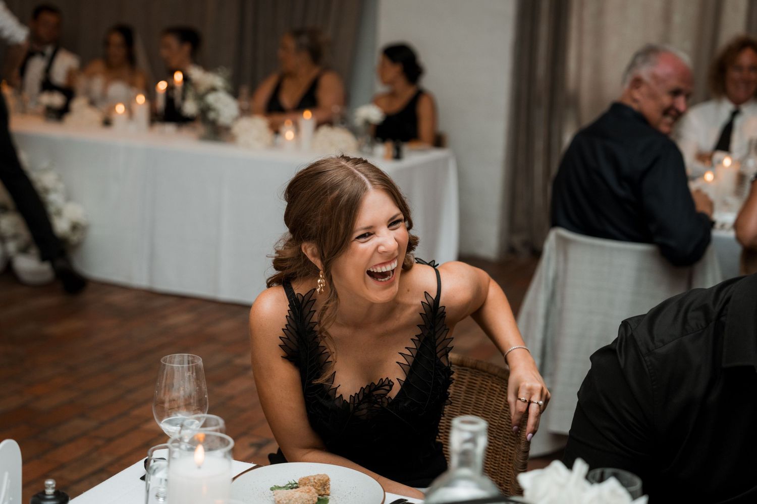 Wedding guests share joyful laughter and conversation during an indoor reception celebration.