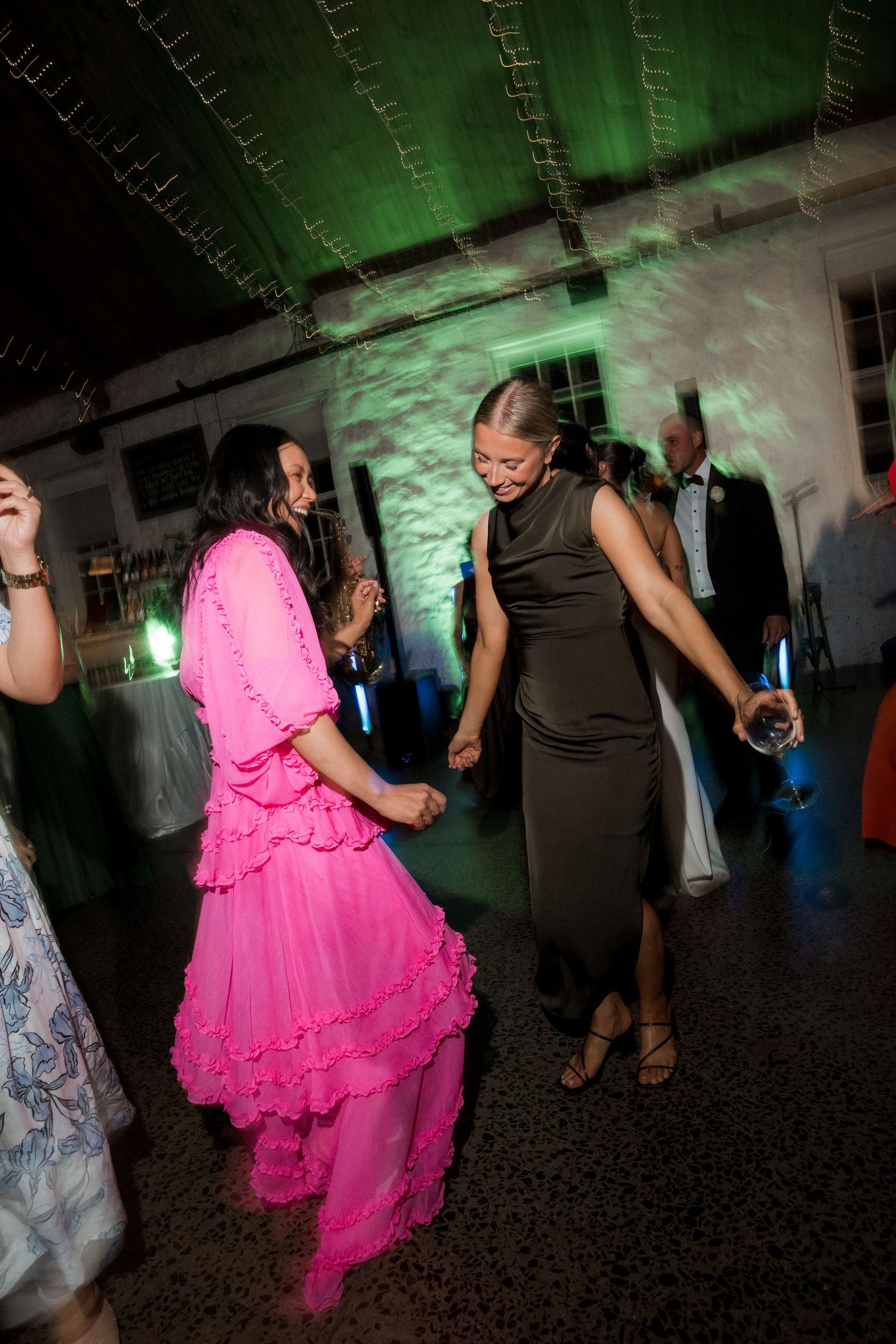 Wedding reception dance floor with vibrant green lighting and guests in colorful attire.