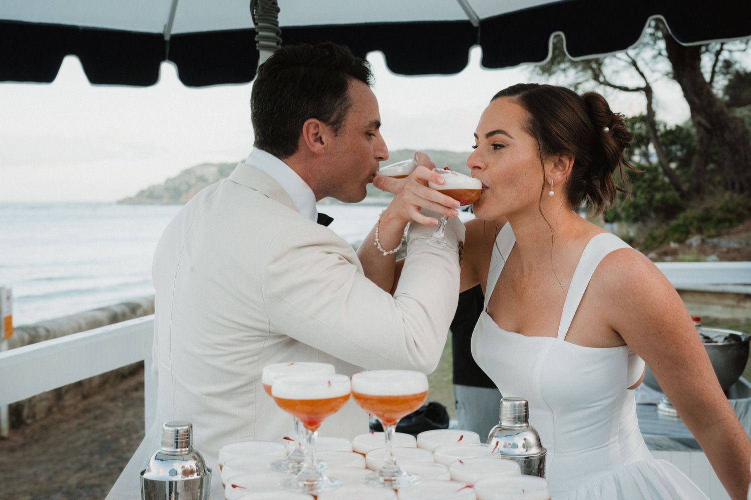 A couple shares an intimate moment under a white umbrella by the ocean on their wedding day.