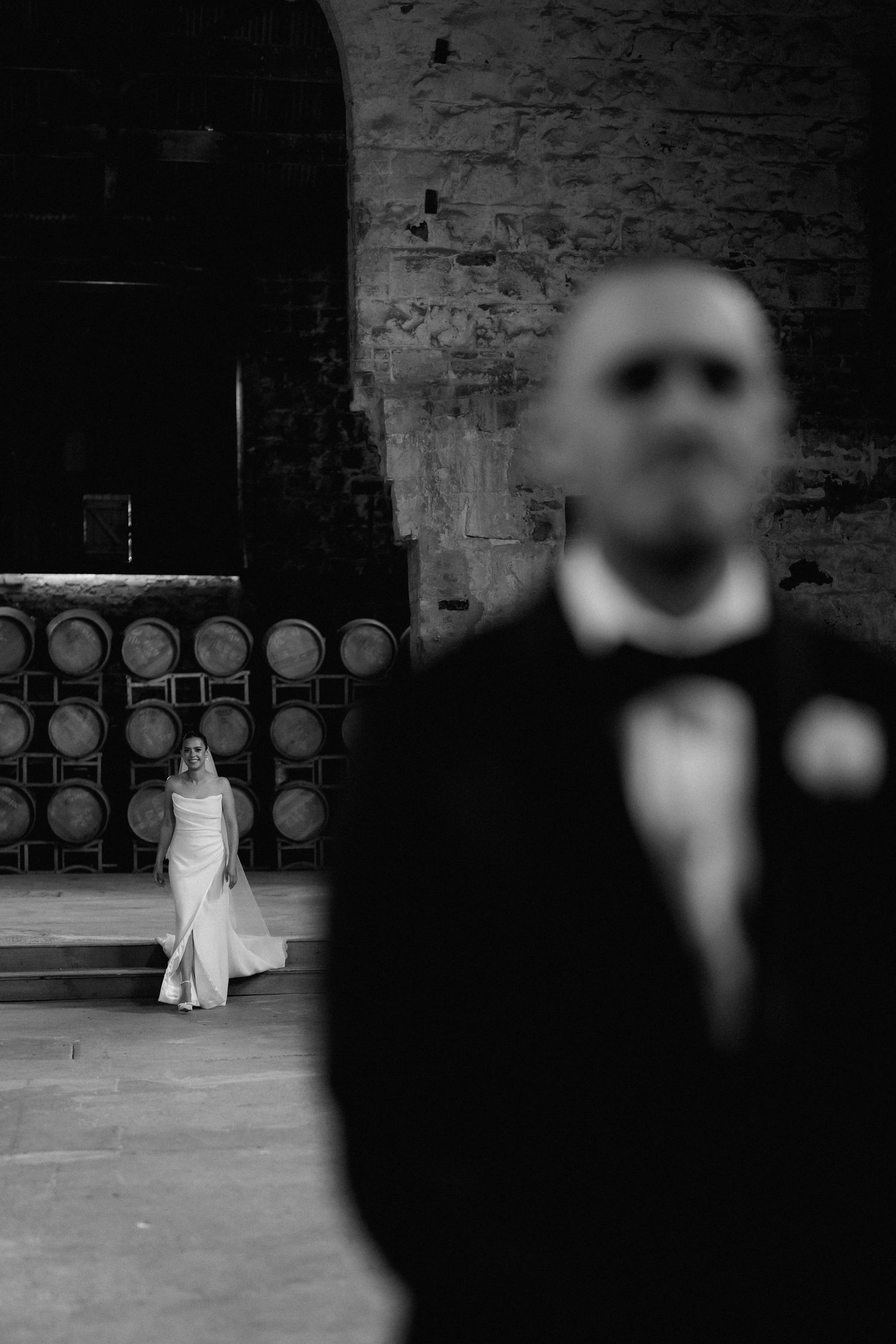 A wedding ceremony setting in a rustic brick venue with wine barrels lining the wall.
