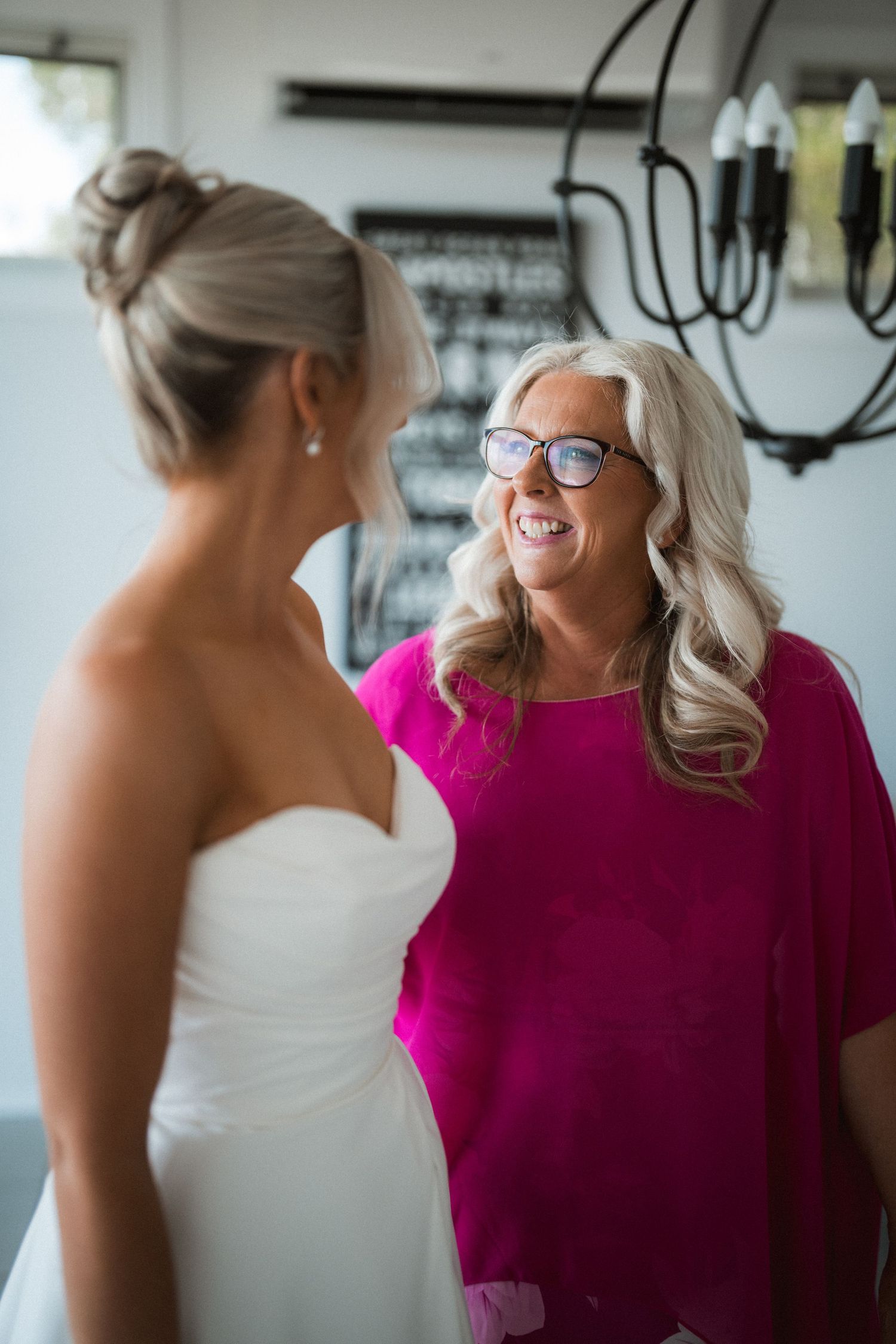 A touching pre-wedding moment between a bride in a strapless gown and a woman in a vibrant pink dress.
