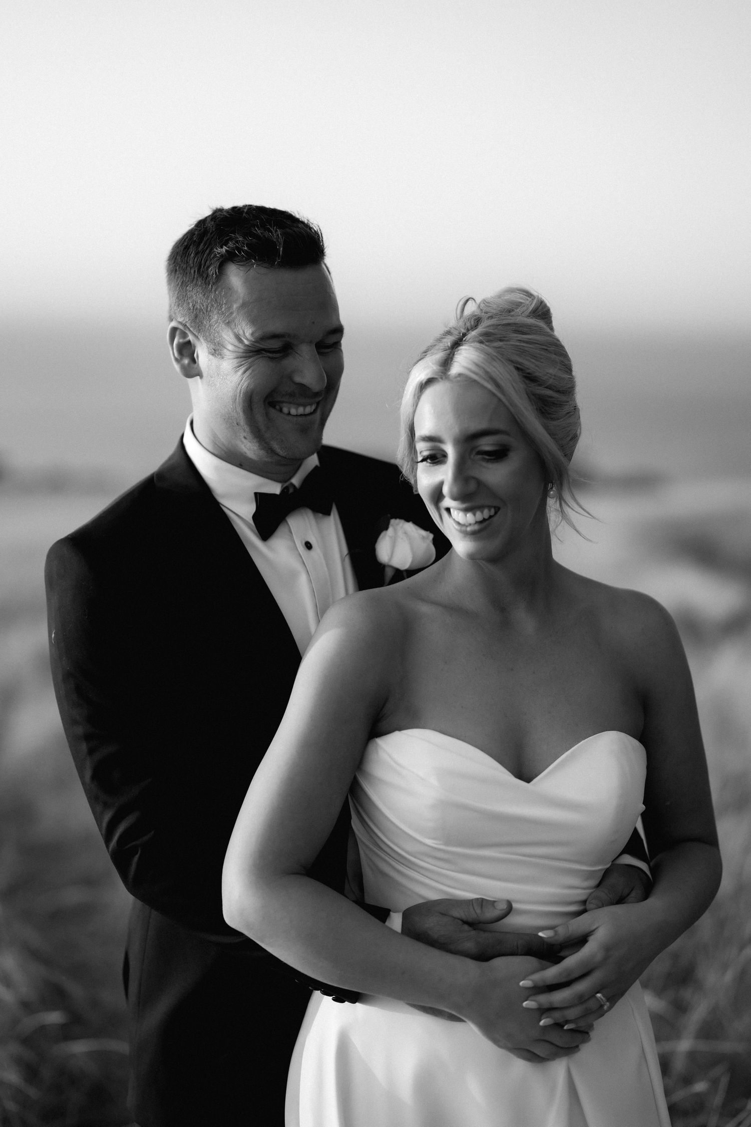 A black and white portrait captures a tender moment between newlyweds embracing outdoors.