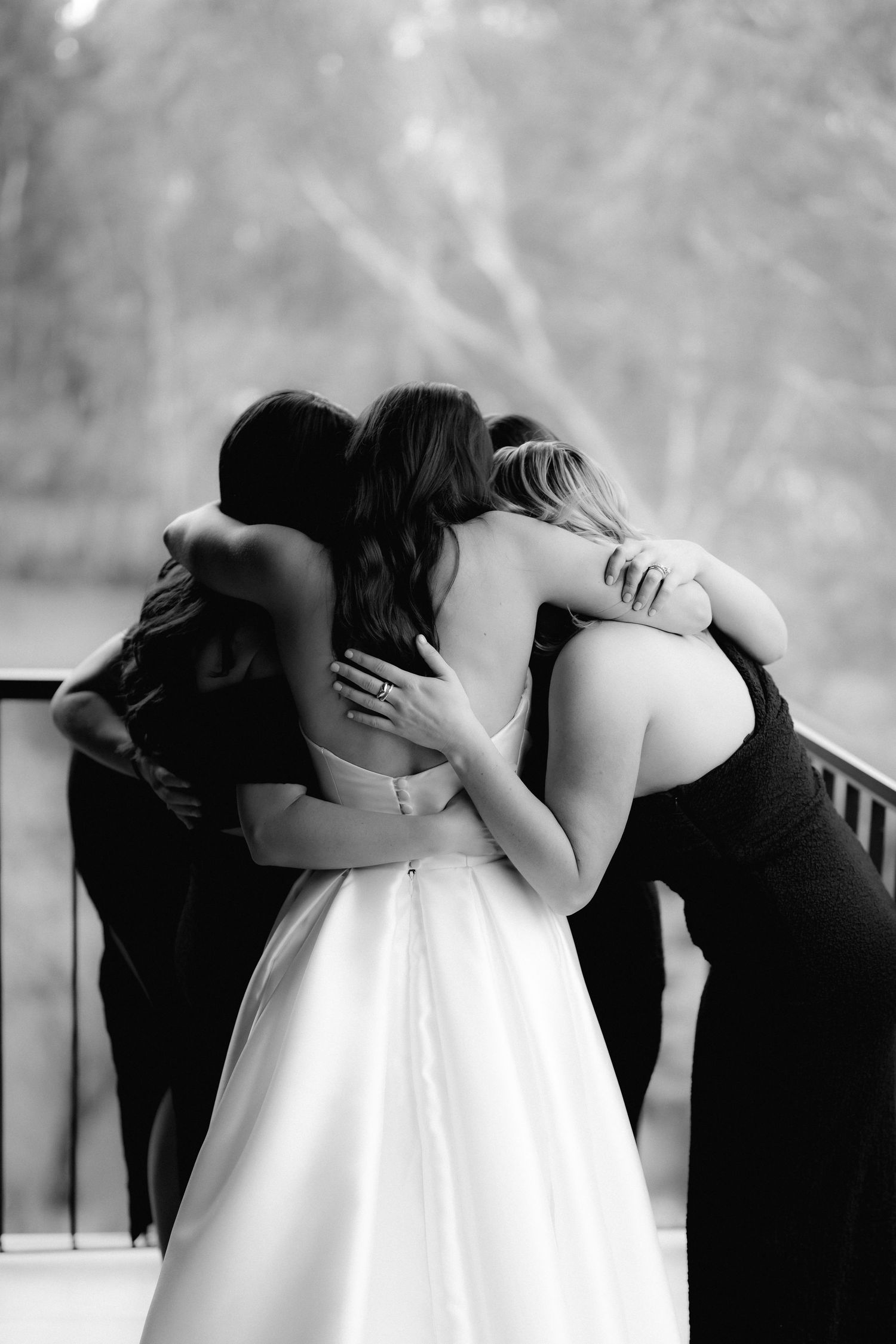 Black and white photo capturing emotional group hug between bride and bridesmaids.