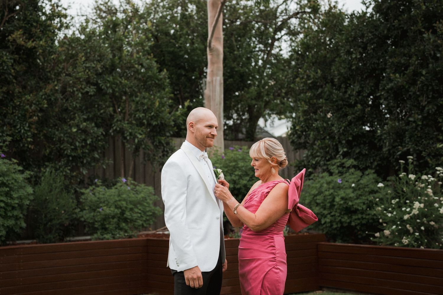 Two people in formal attire share a joyful moment on a wooden deck surrounded by lush greenery.