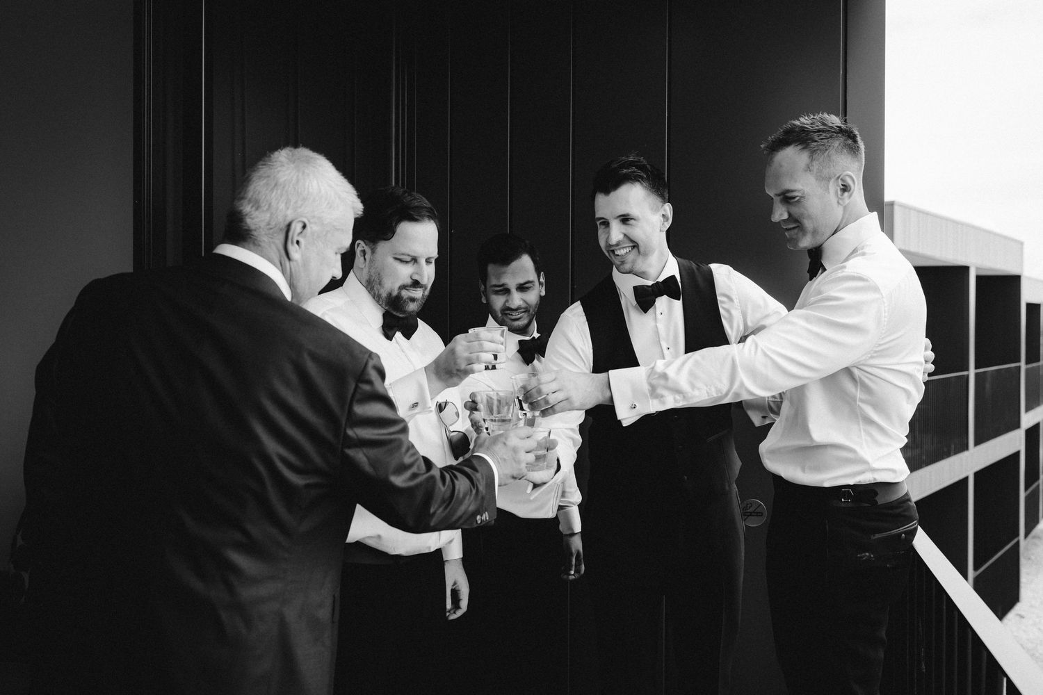 A group in formal black and white attire gather together sharing a lighthearted moment in a bright indoor space.