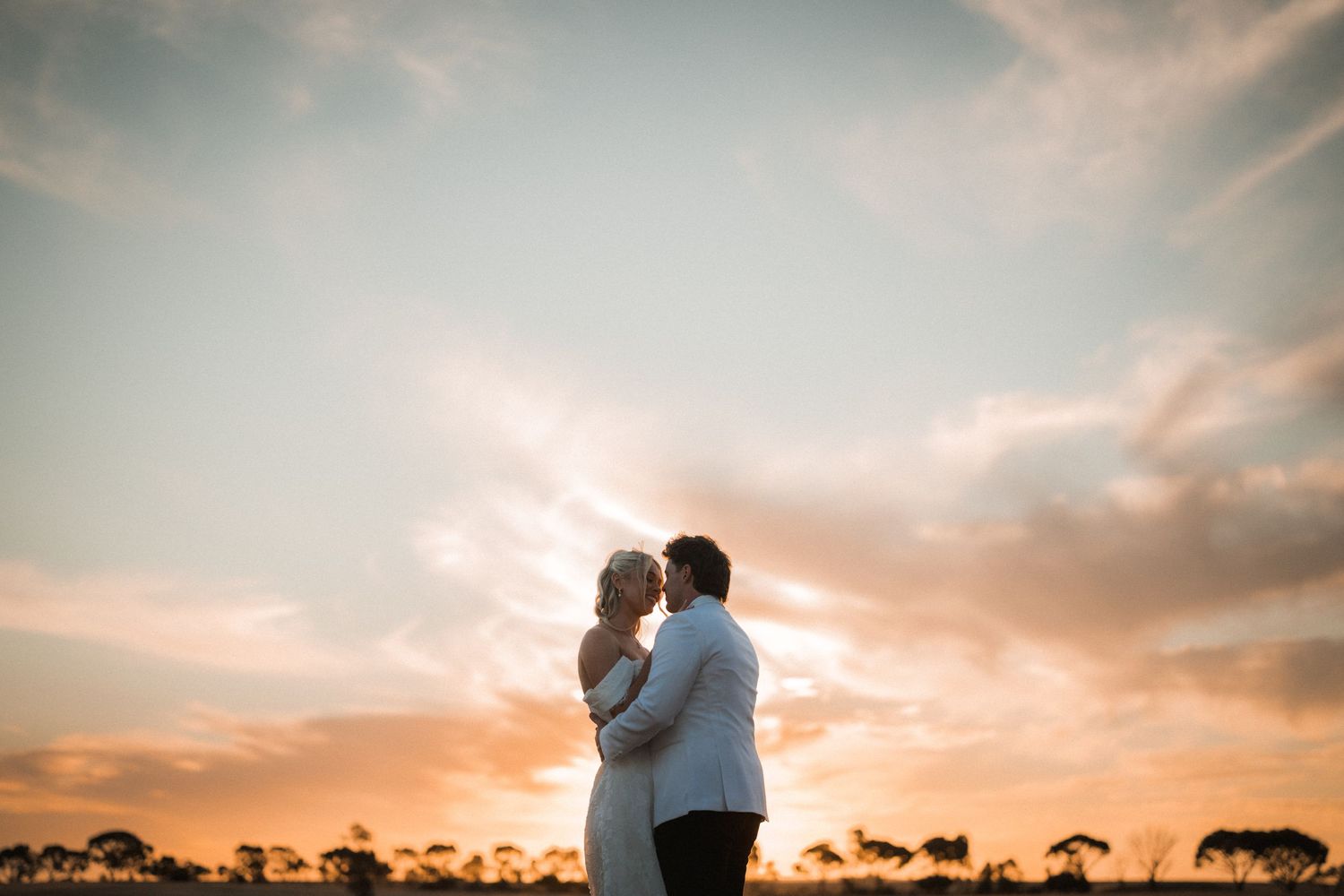 Couple sharing romantic kiss silhouetted against vibrant golden sunset sky.