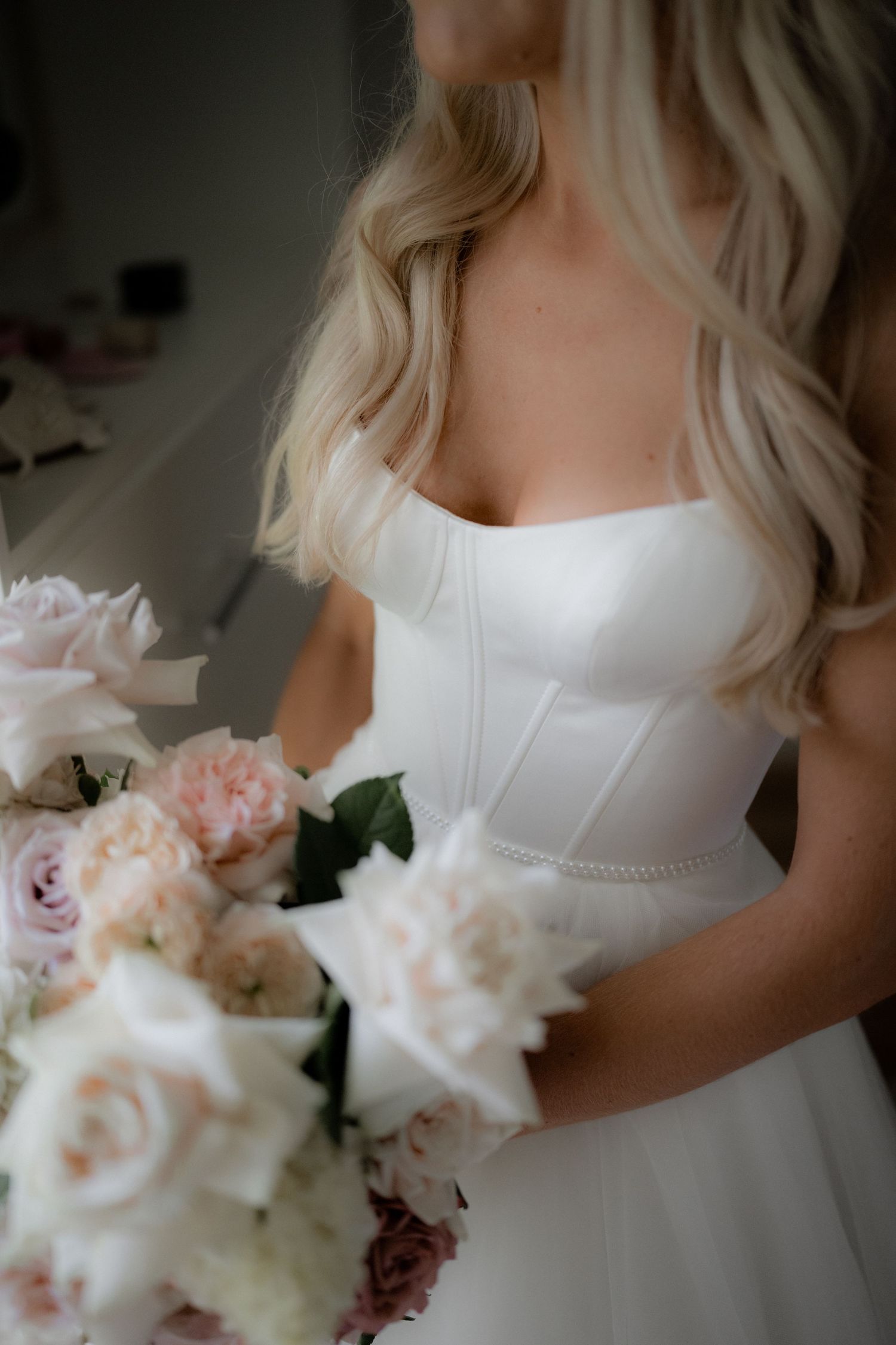 Close-up details of a white bridal bouquet with soft pink and white roses against a light background.