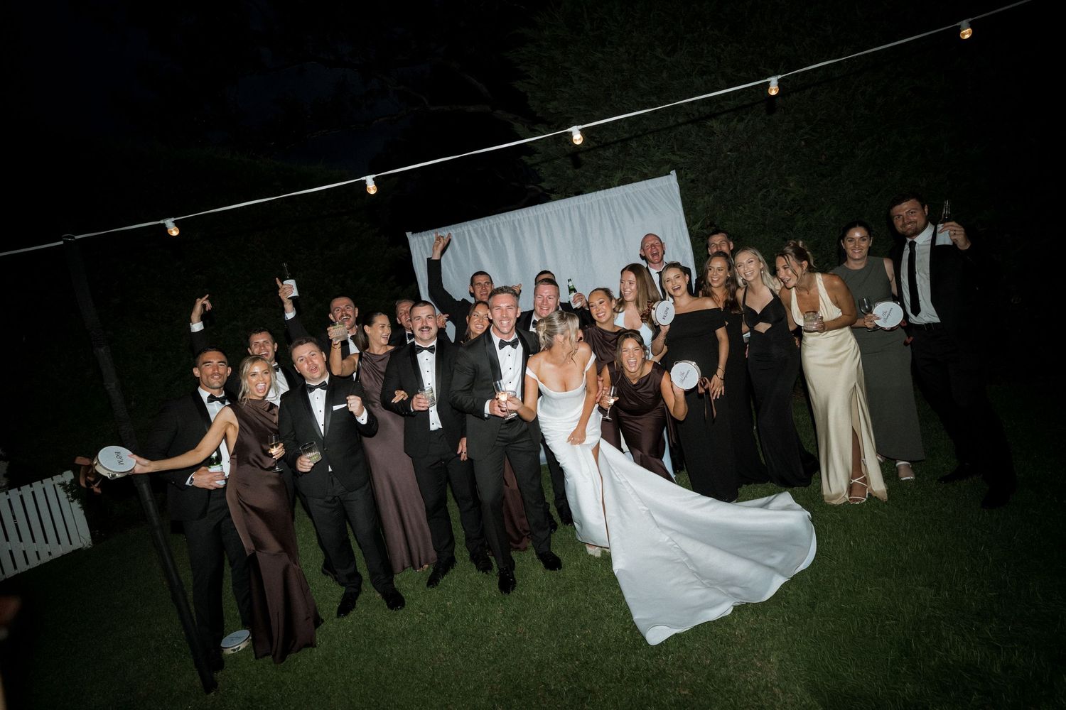 Wedding guests watch as a bride and groom dance together during their first dance at an outdoor evening reception.