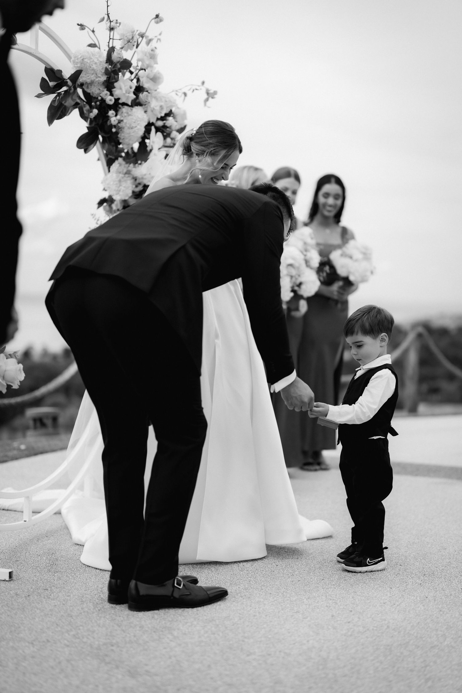 A heartwarming black and white wedding moment with a small ring bearer holding onto the bride's dress.