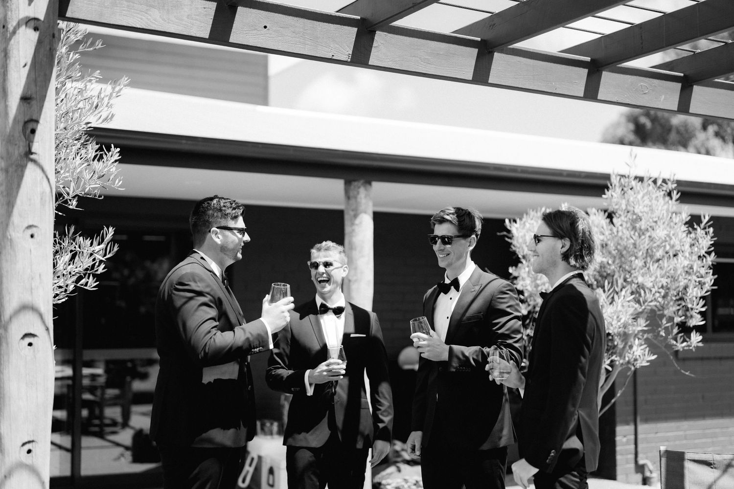 Wedding party members enjoy drinks and conversation on an outdoor patio.