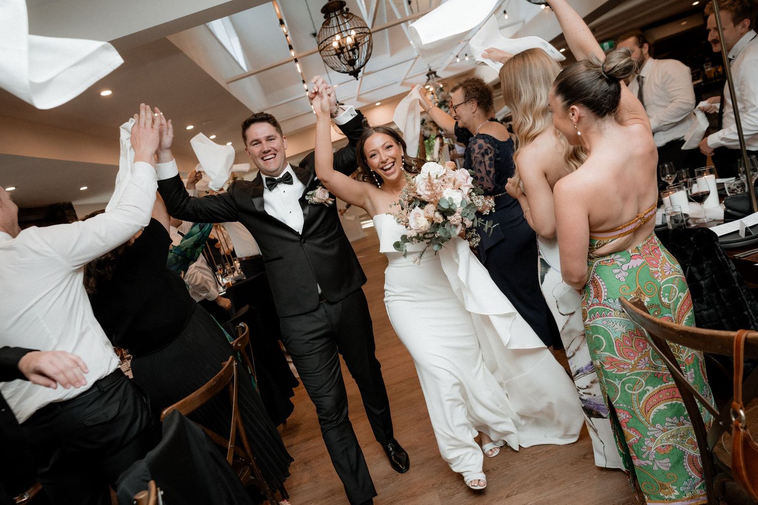 Energetic wedding reception celebration with guests cheering and dancing.