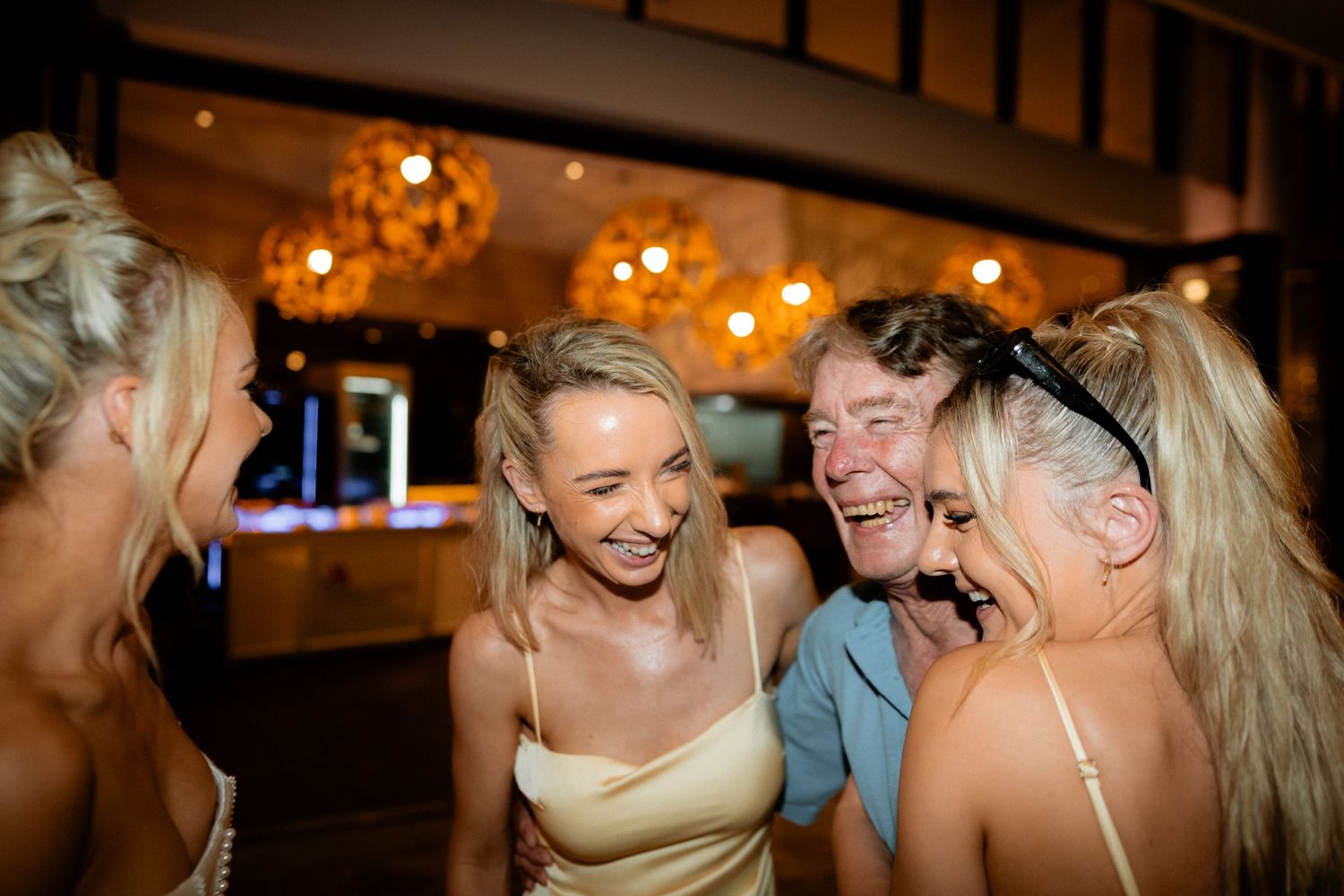 Friends sharing joyful laughter at an evening reception with warm lighting.