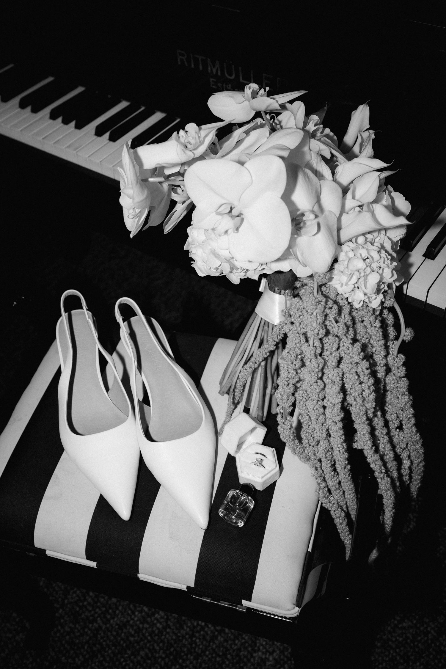 Black and white photo of white platform heels next to a floral bouquet displayed on piano keys.