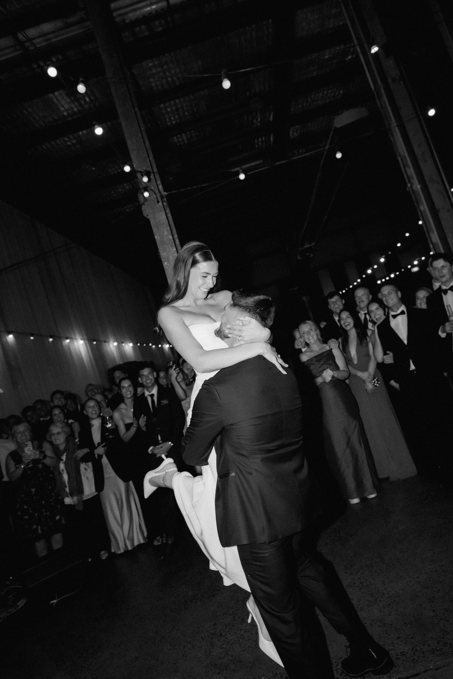 A couple performs a dramatic dip during their first dance at a wedding reception with string lights overhead.