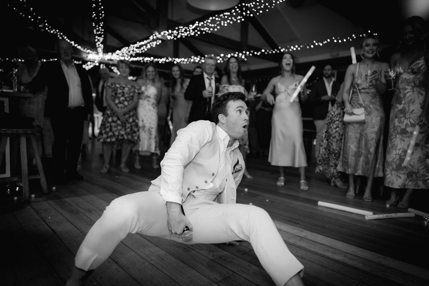 Black and white photo of a lively dance floor celebration with string lights above.
