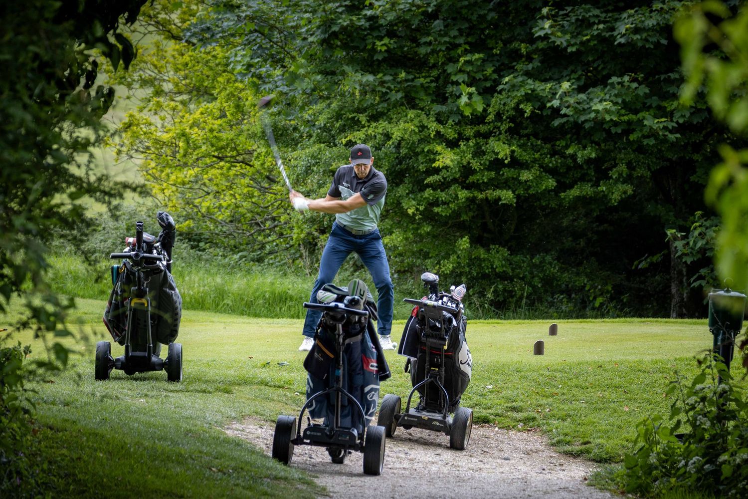 Golfer teeing off framed by golf trolleys in the foreground on a lush course in Sussex, England, golf photography