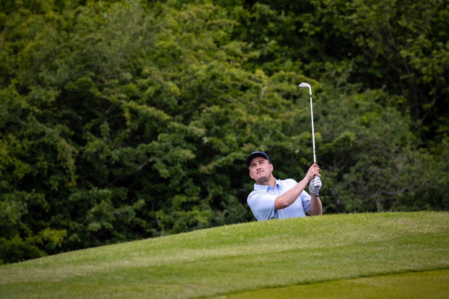 Golfer playing an approach shot on a lush golf course in the Sussex countryside, golf action photography