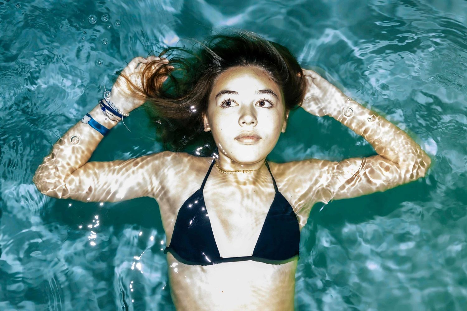 A portrait of a young lady floating in the blue waters of a swimming pool illuminated by flash - 
Algarve Portrait Photography