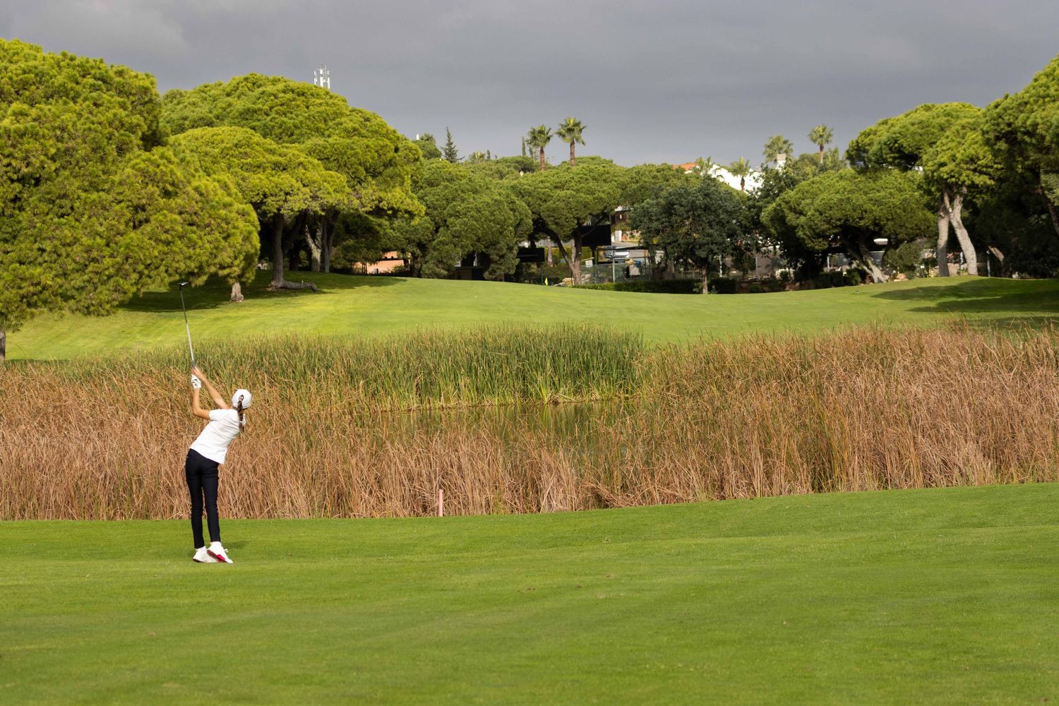 Young golfer playing a fairway shot on a par 5 hole surrounded by reed beds on an Algarve golf course
