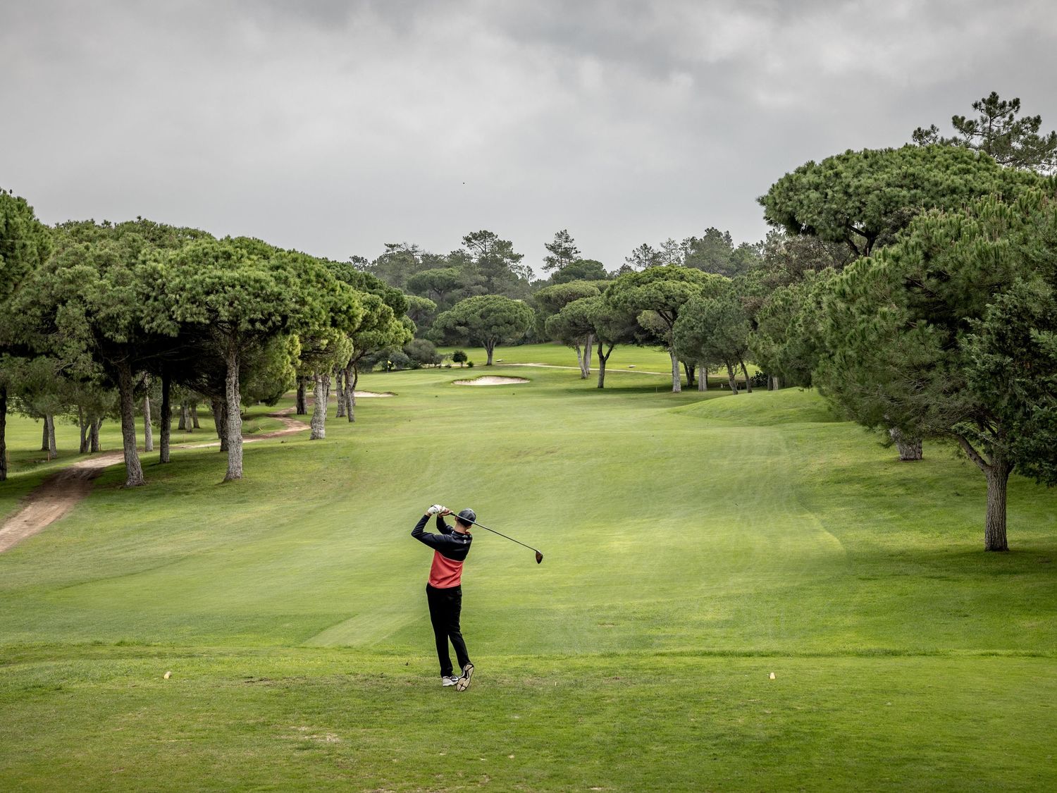 Young golfer teeing off on a tree-lined golf course in the Algarve, Portugal golf action photography