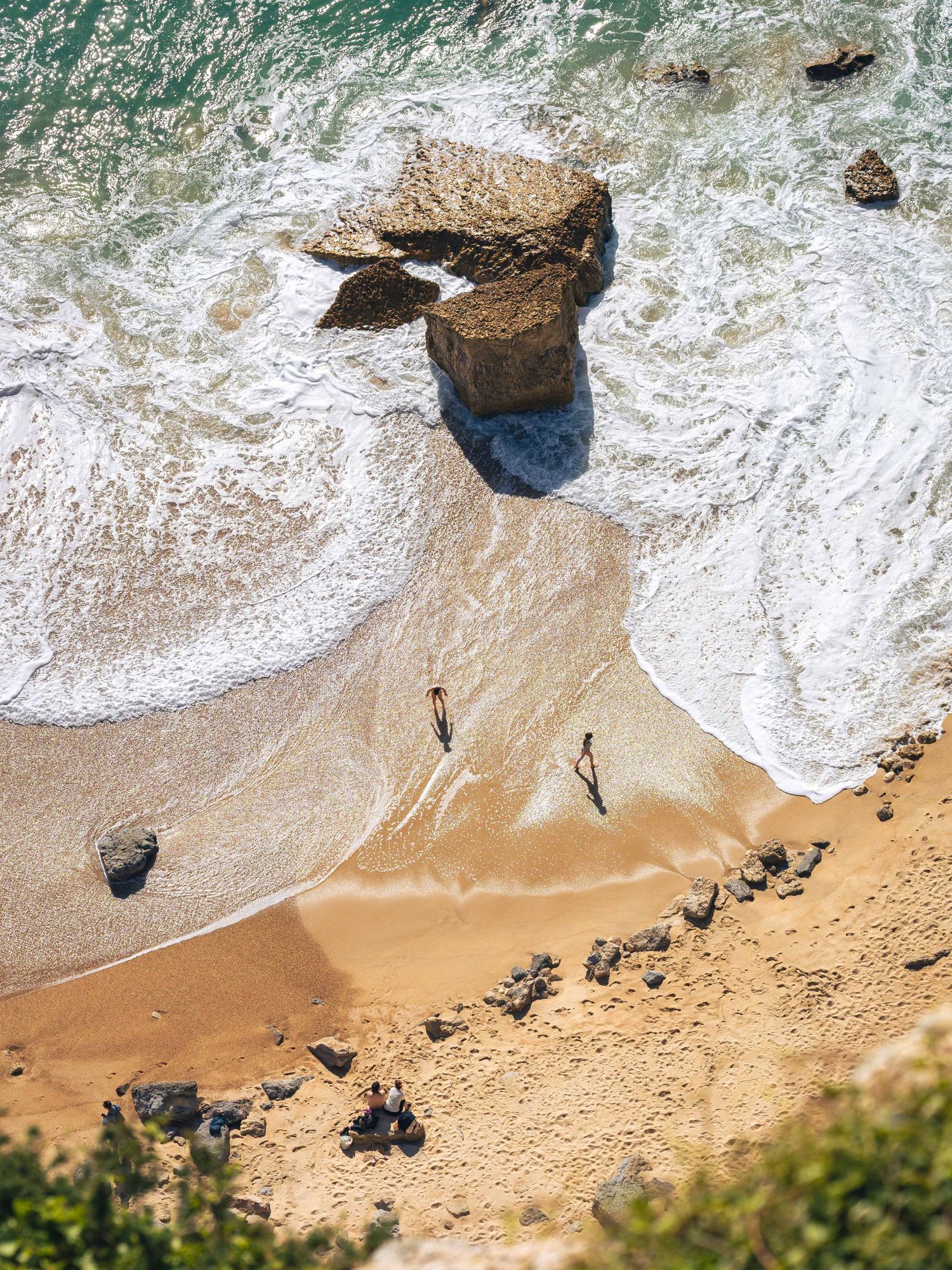 Clifftop view of people playing in the waves on a golden beach at Nazaré, Portugal, fine art travel photography