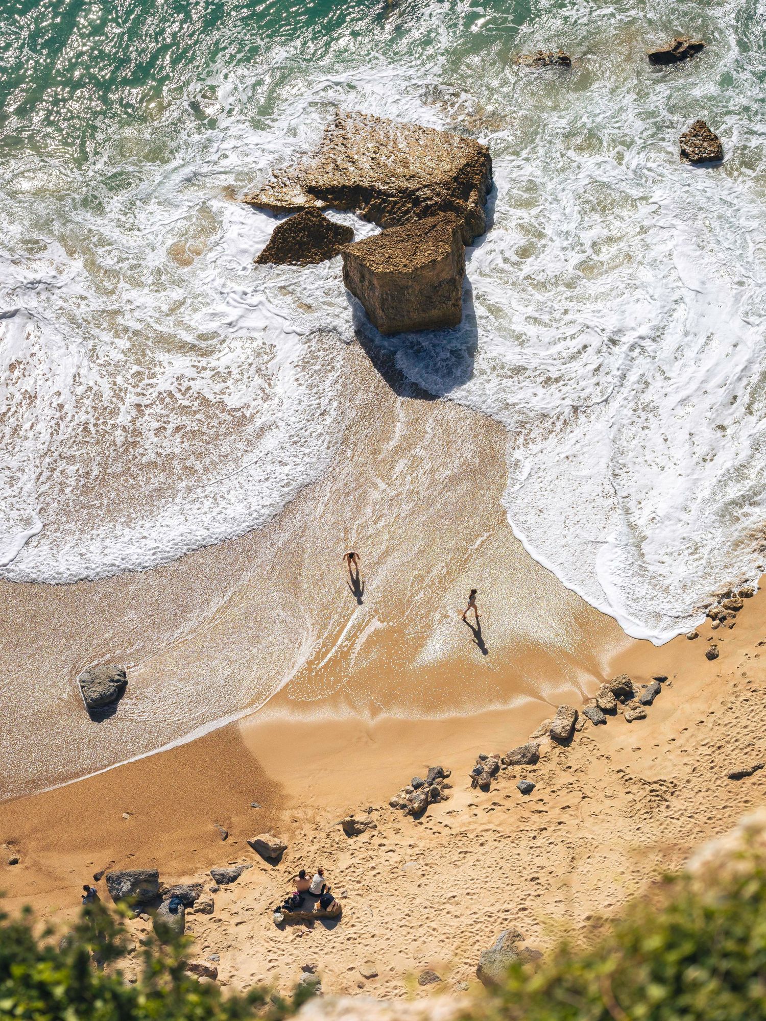 Clifftop view of people playing in the waves on a golden beach at Nazaré, Portugal, fine art travel photography