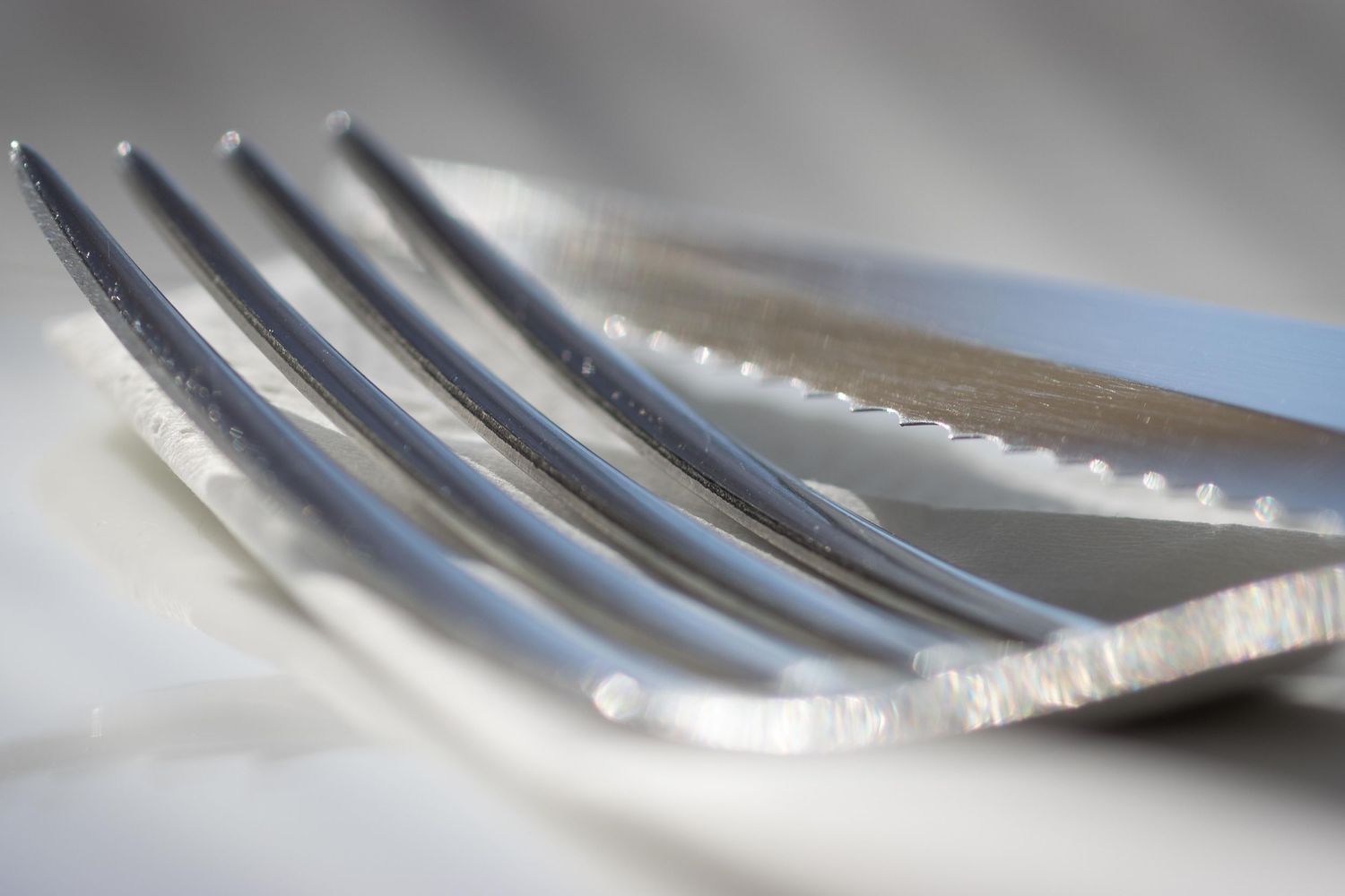 Close-up macro shot of a silver fork and knife on a white tablecloth, restaurant photography by Anthony West