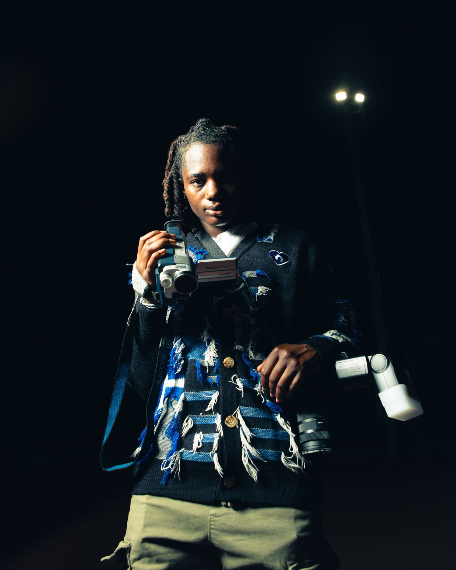 Young man holding camera equipment poses dramatically under stage lighting.