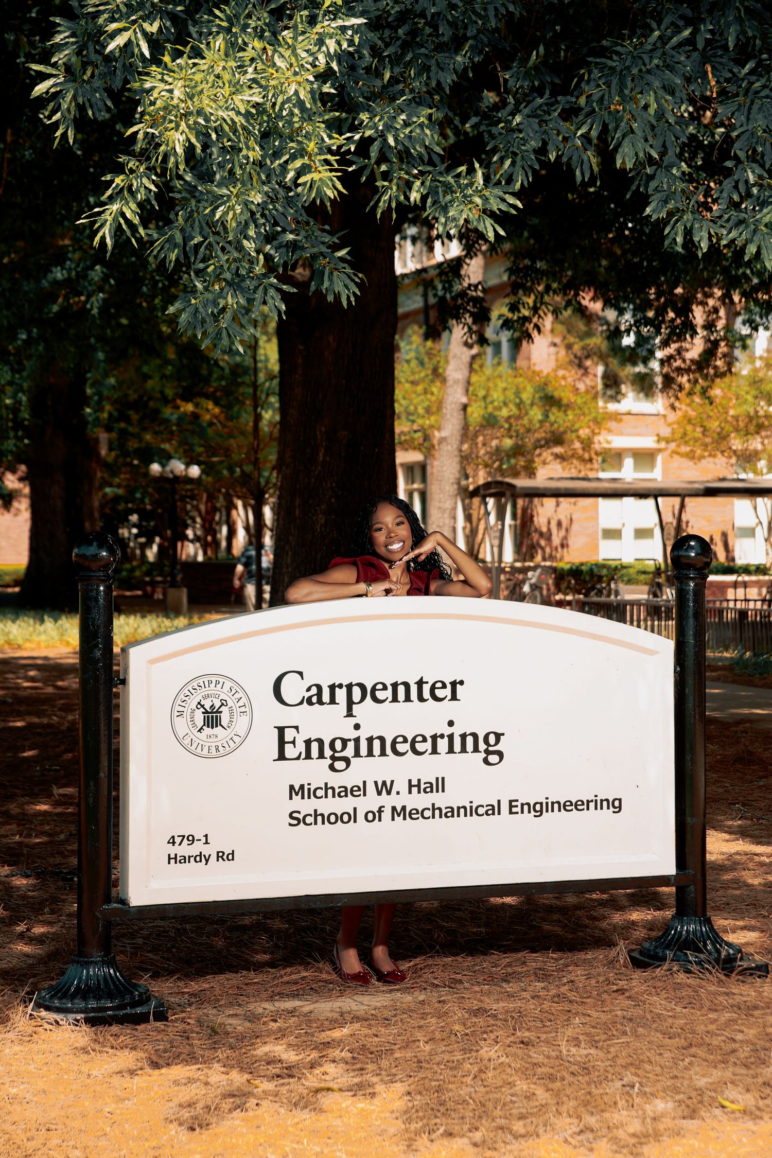 Student poses behind Carpenter Engineering Michael W. Hall School sign on campus.