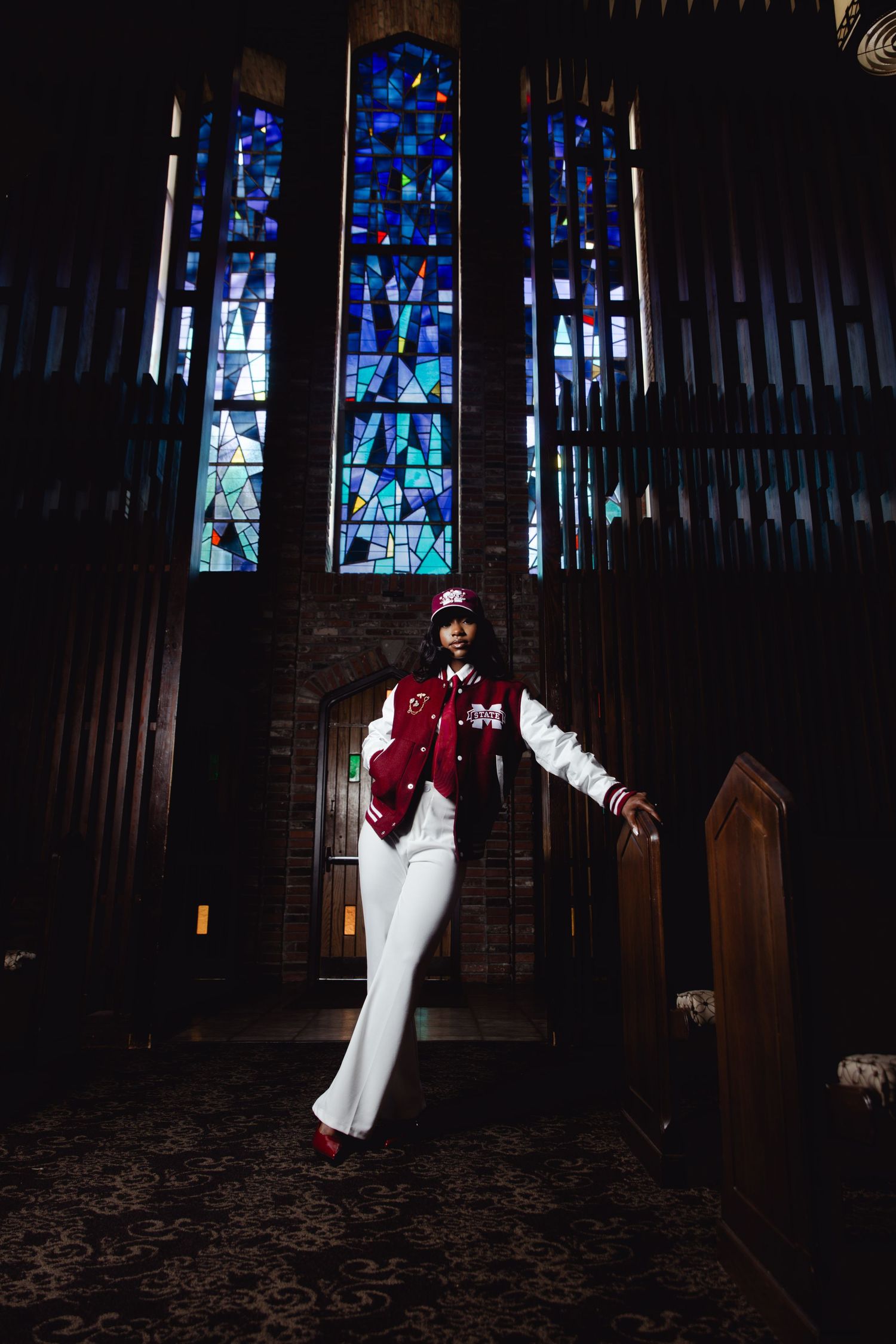 Student in Mississippi State varsity jacket poses in chapel with stained glass windows.