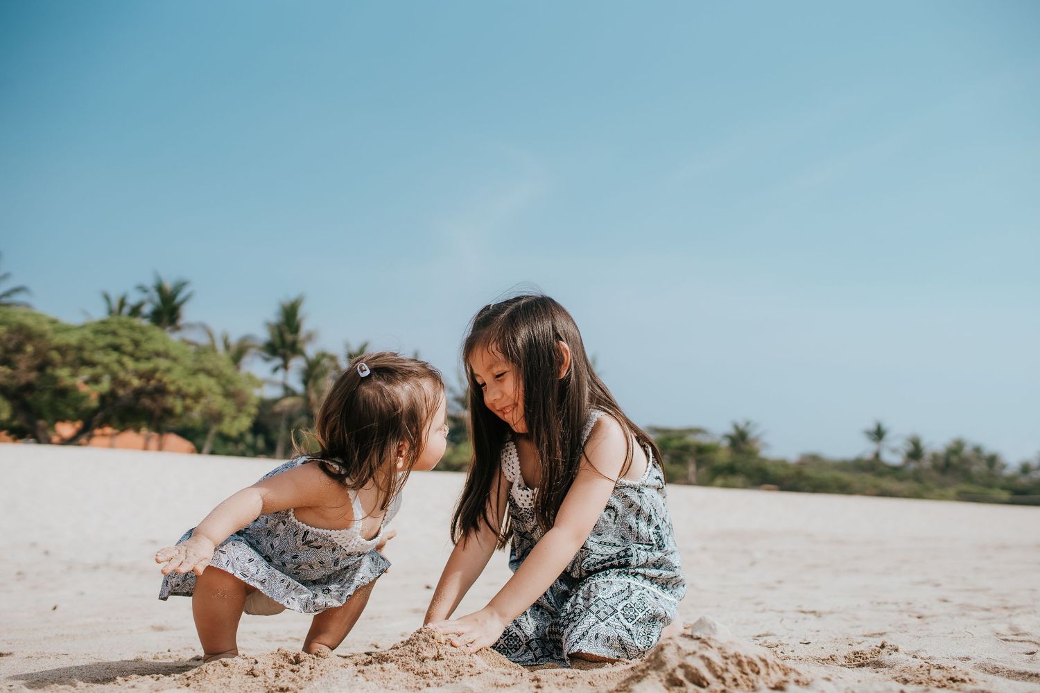 Two children playing together in the sand on a sunny tropical beach.