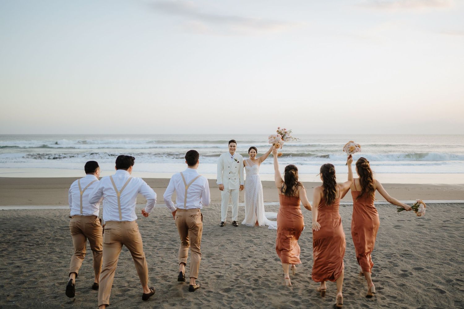 Group of friends in coordinated outfits running and playing on a beach at sunset.