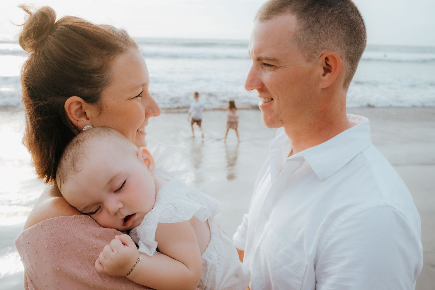 An intimate family moment captured on the beach with a sleeping baby.