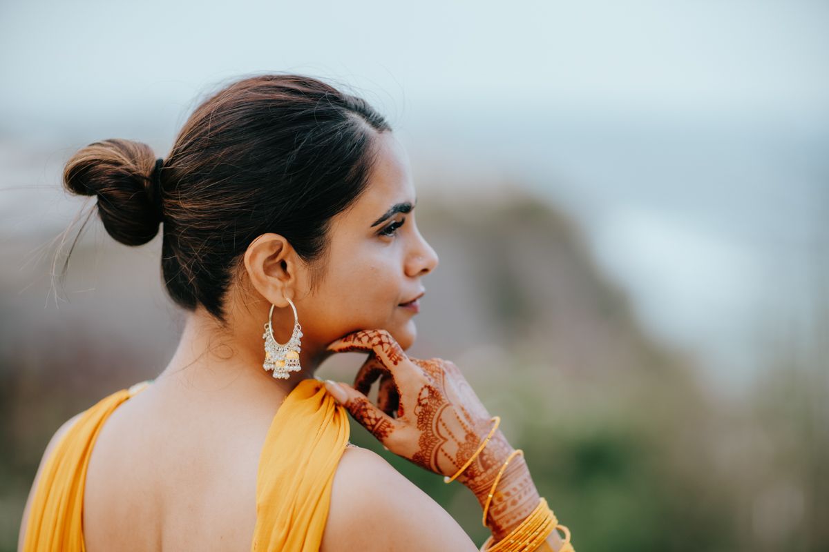 Side profile portrait of someone wearing a yellow outfit and ornate silver earrings against a light background.