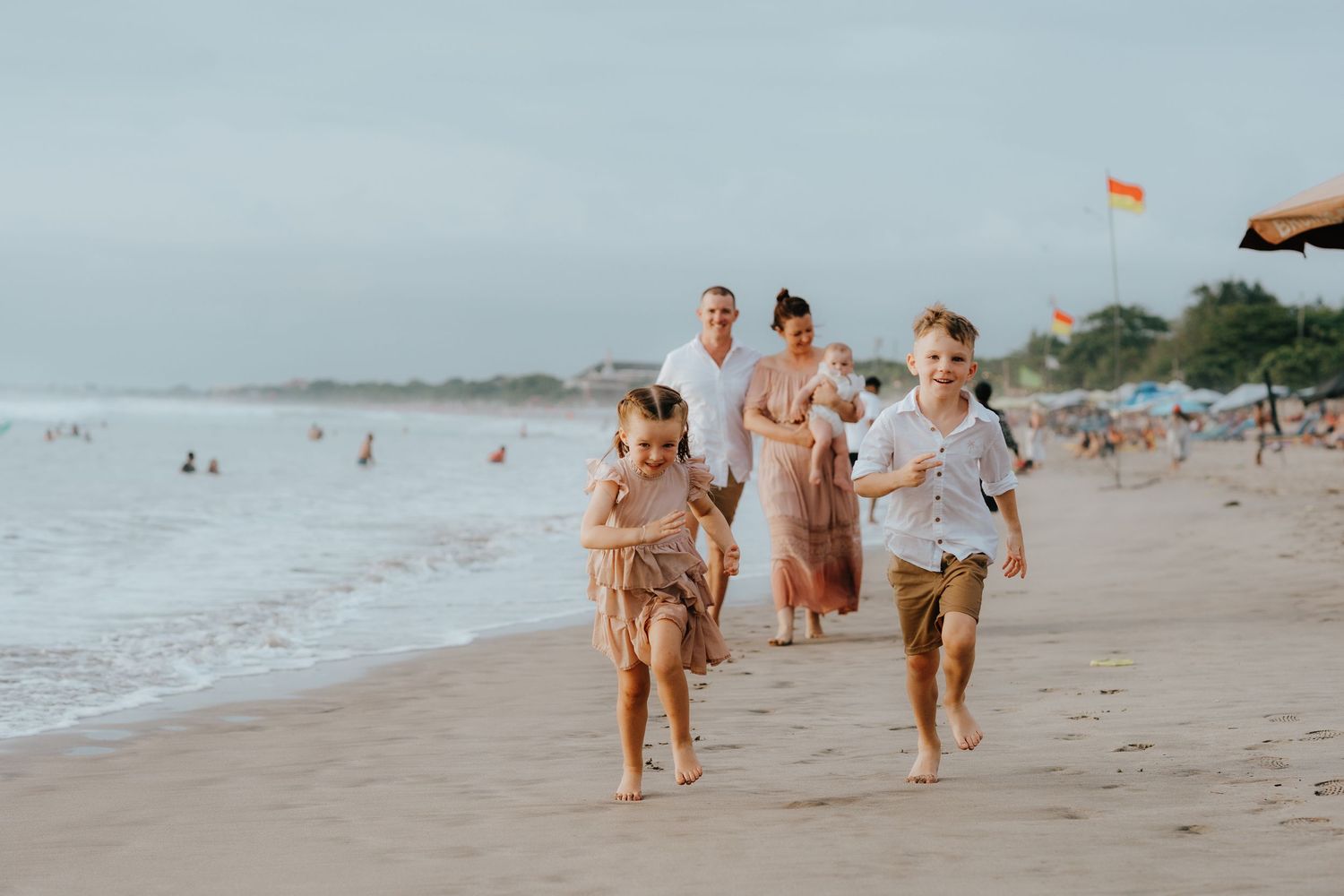 Family members running and playing together along a scenic beach with waves in the background.