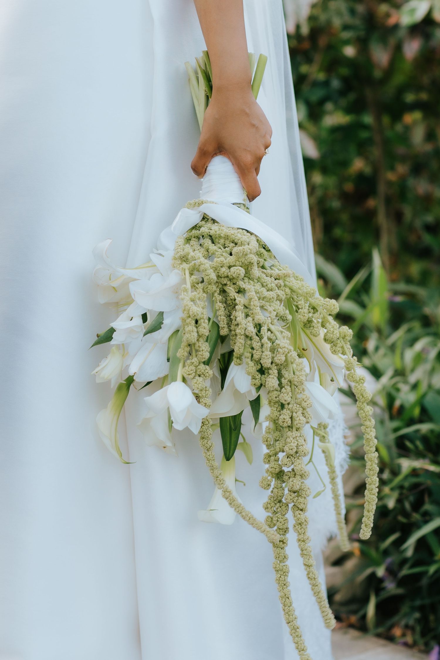 Bride in white dress holding an elegant cascading bouquet of white lilies and green amaranthus flowers.