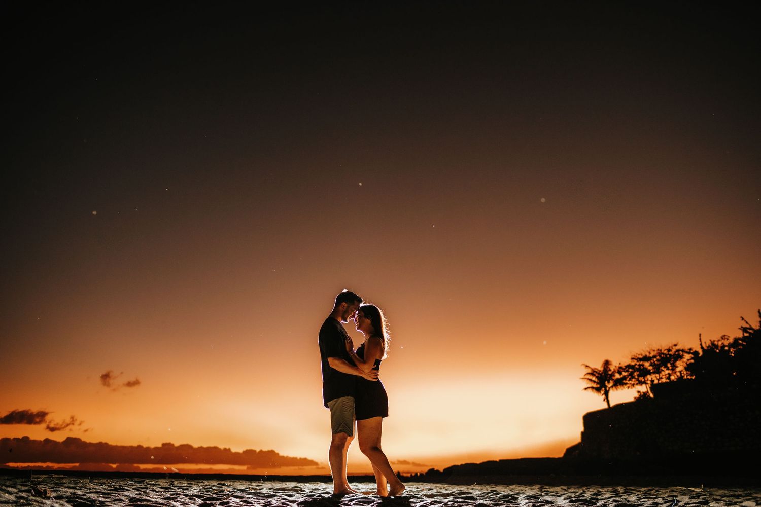 Romantic silhouettes embracing against dramatic sunset backdrop.