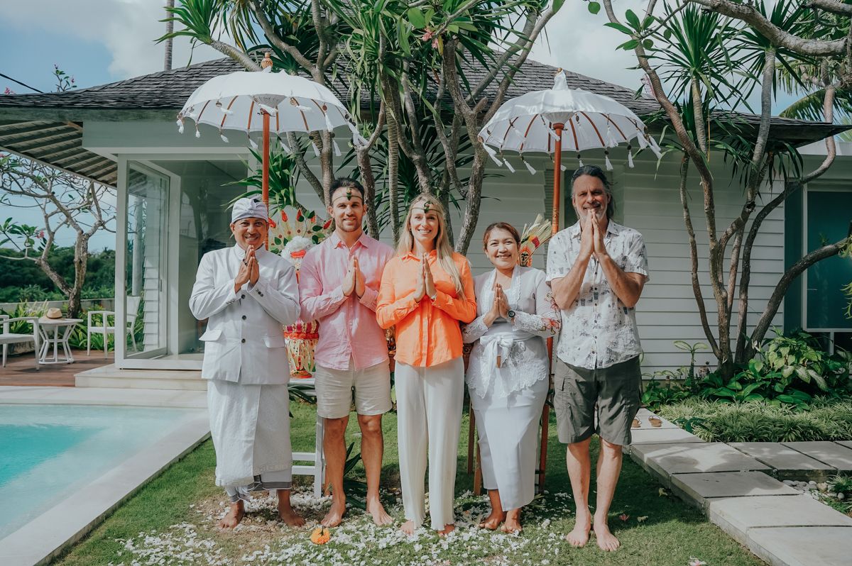 Group photo of celebration attendees in coordinated white and orange outfits by a pool.