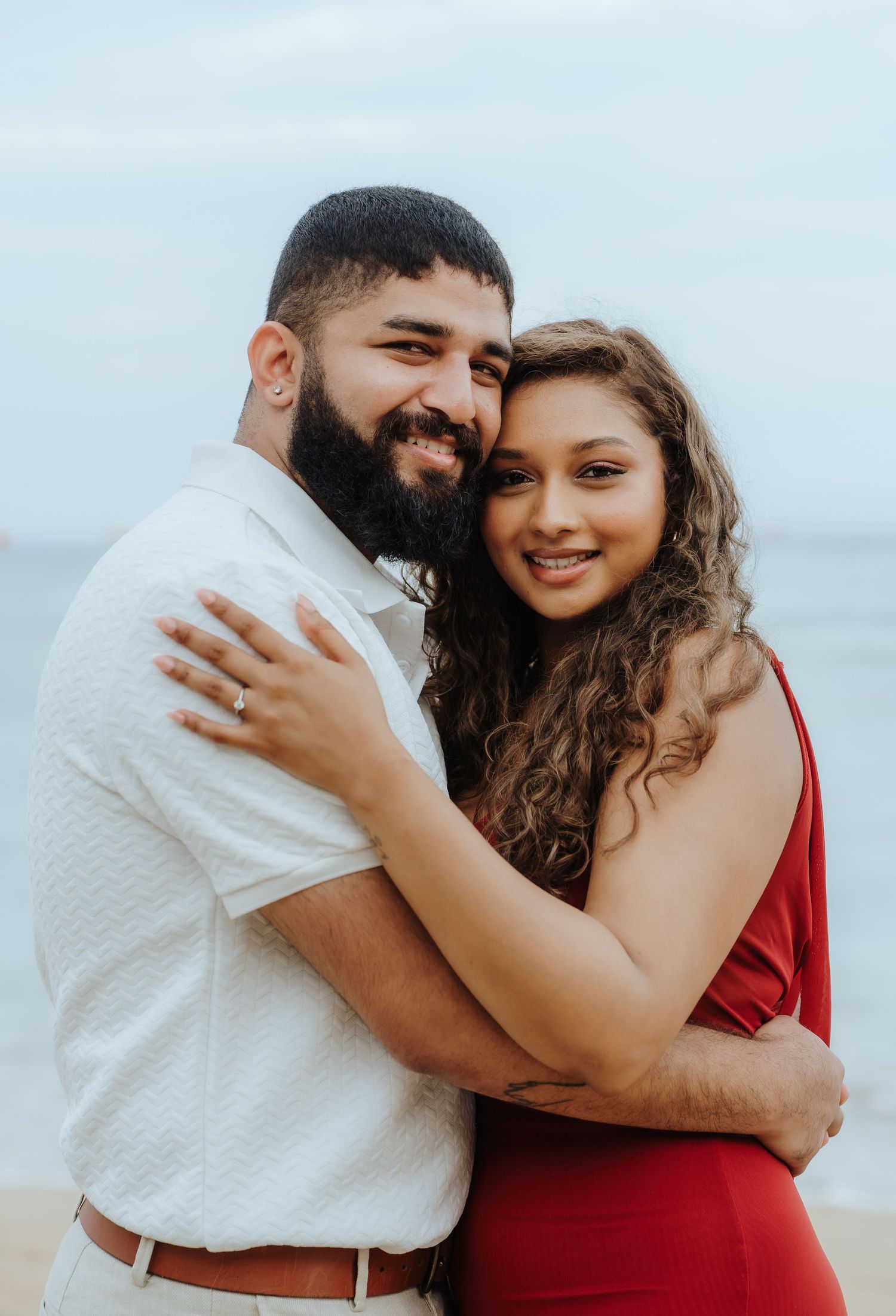 A couple shares a joyful embrace while wearing red and white outfits during a beach photoshoot.