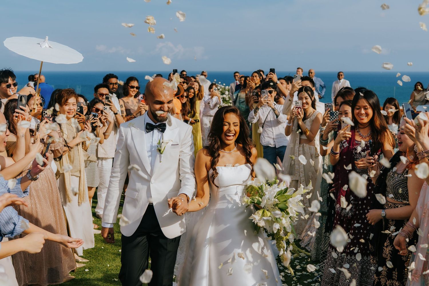 Joyful newlyweds walk down the aisle as guests toss flower petals at an elegant outdoor wedding ceremony.