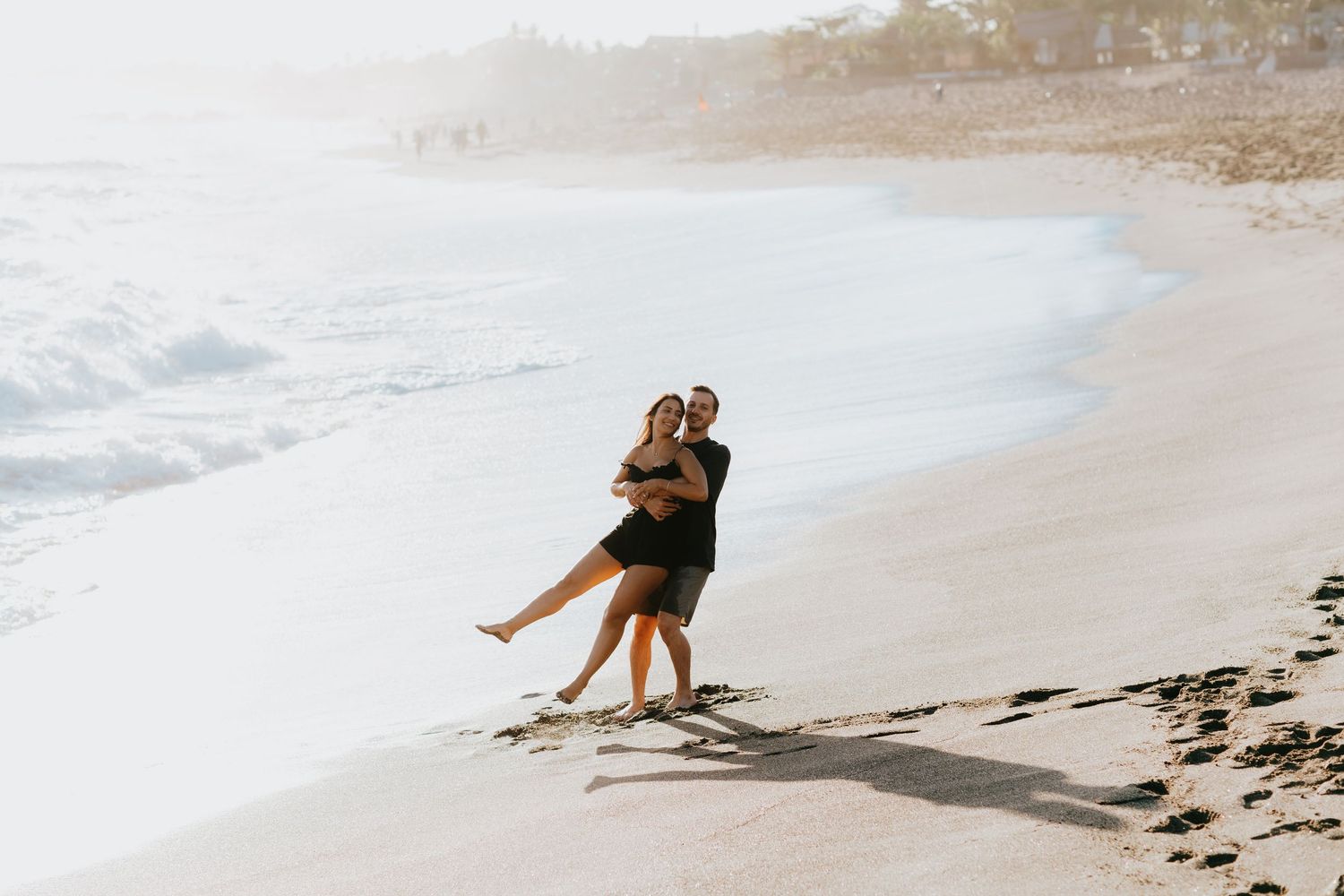 Two people enjoying a romantic moment on a sandy beach with waves crashing nearby.