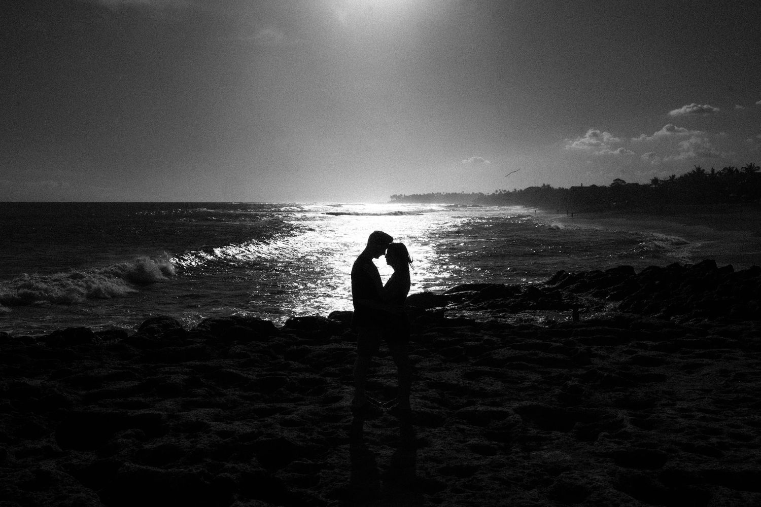 Silhouetted figures on beach at sunset creating romantic black and white panoramic scene.