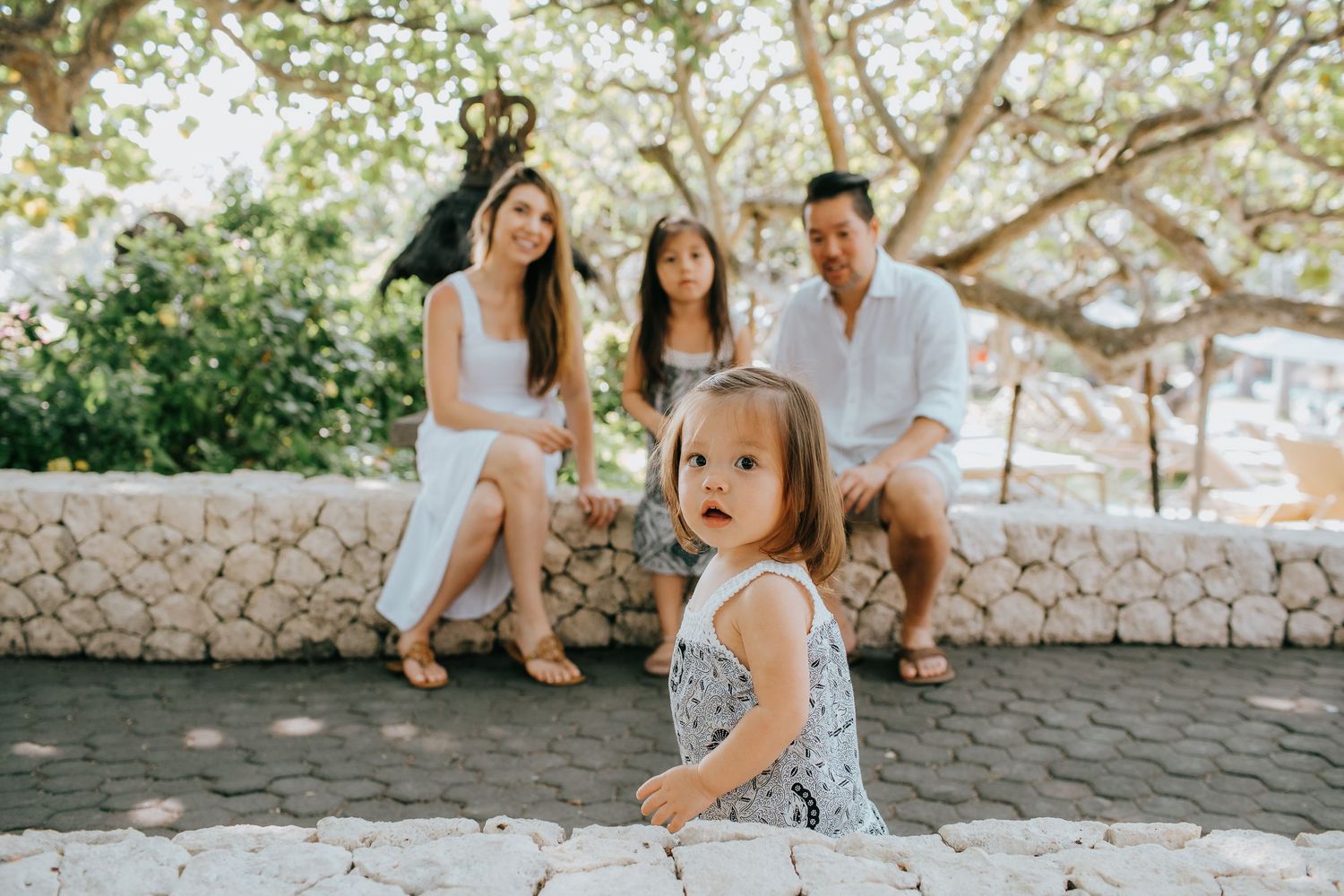 Family enjoying a sunny day together on stone steps surrounded by trees.