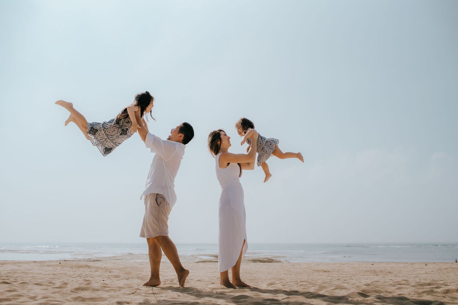 Parents playfully lifting children in the air at the beach.